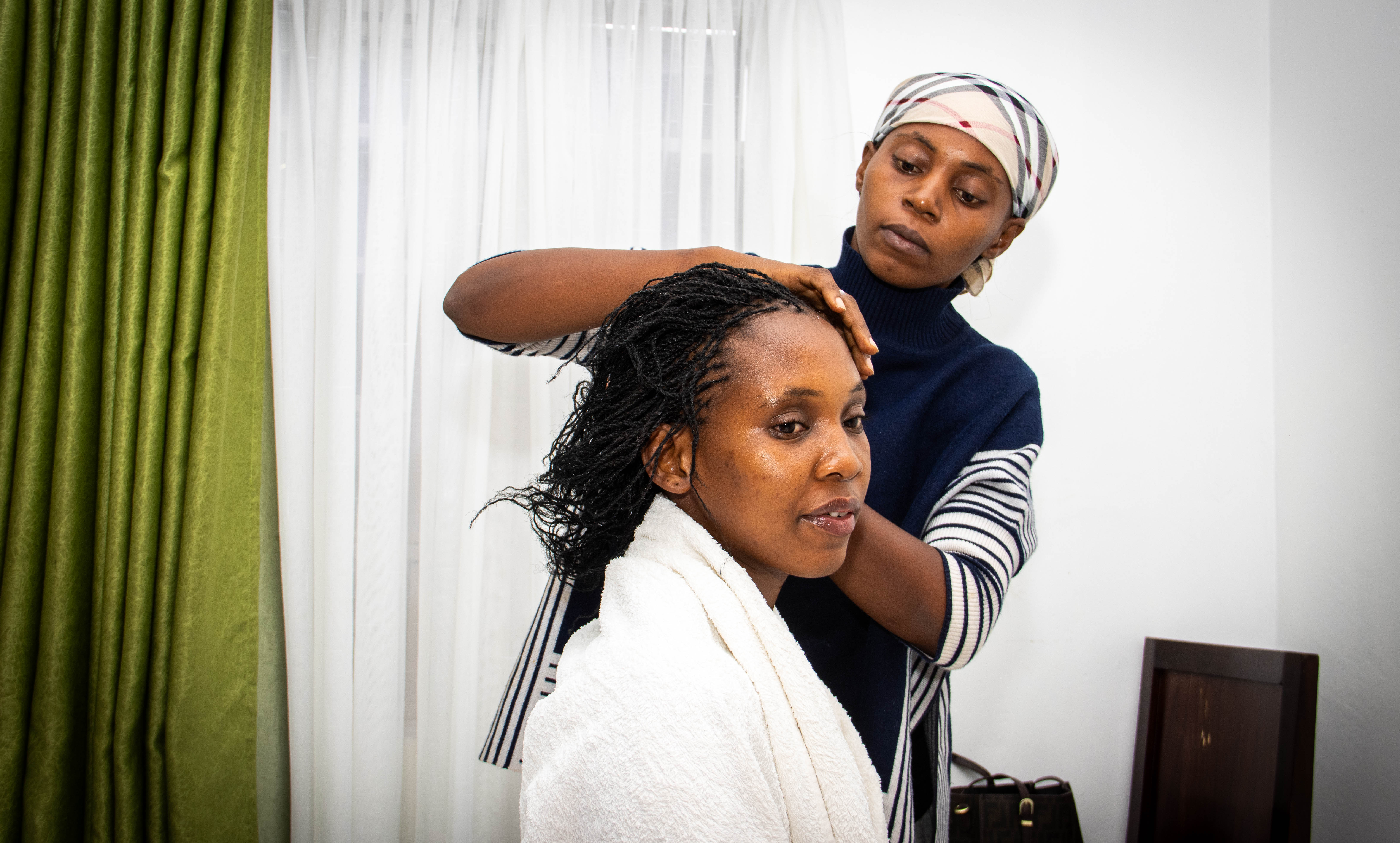 A stylist works on the bride's hair beside a window