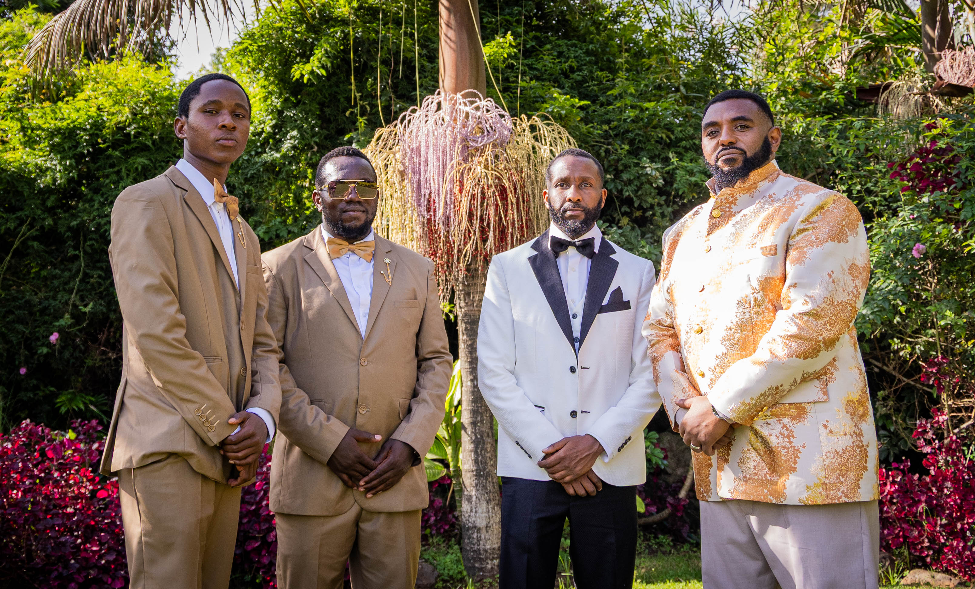 The groom and three groomsmen in suits stand in a lush garden