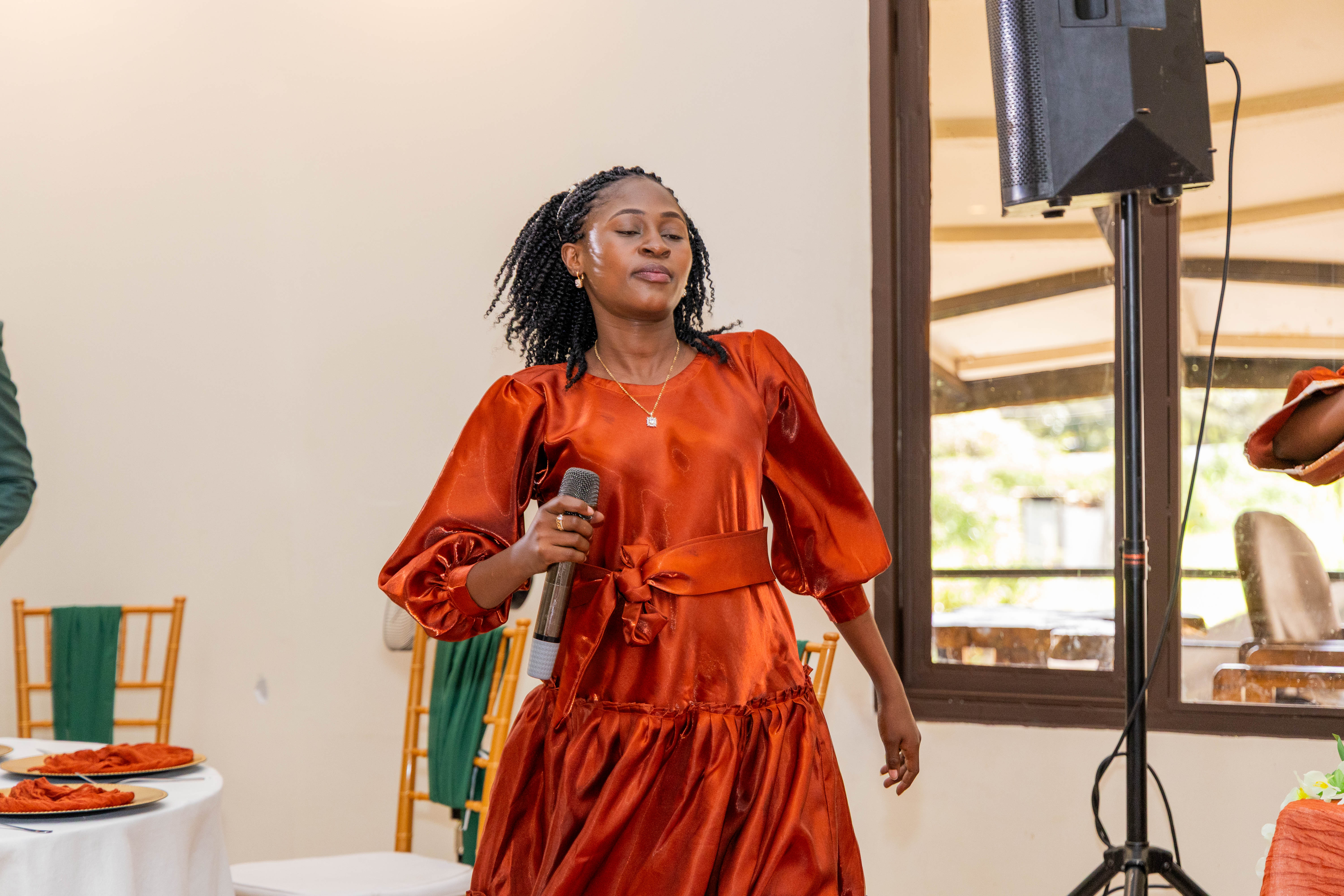 A woman in a rust-coloured dress sings into a microphone at the reception
