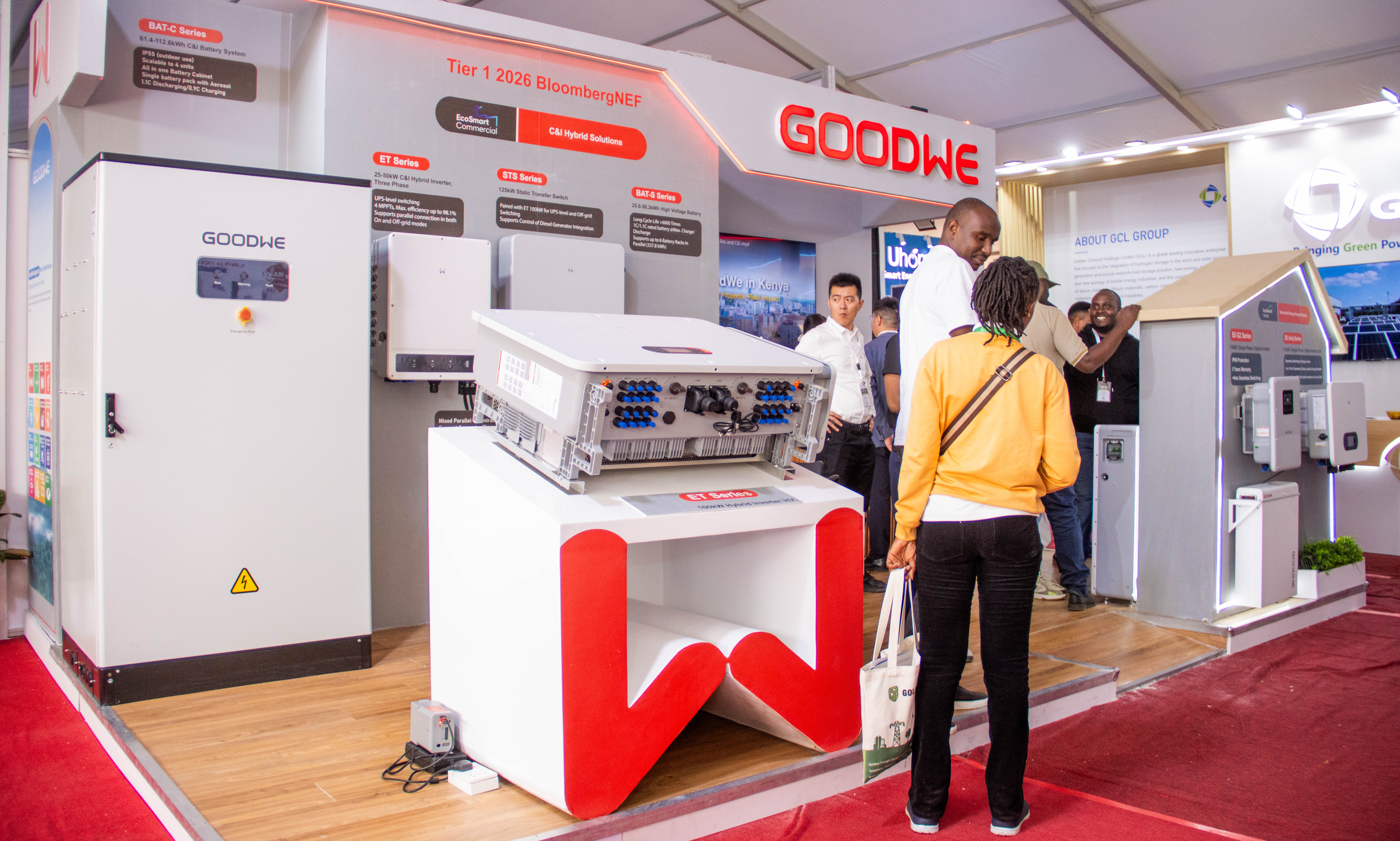 A wide view of a red and white expo stand with battery cabinets, inverters and a visitor in a yellow top