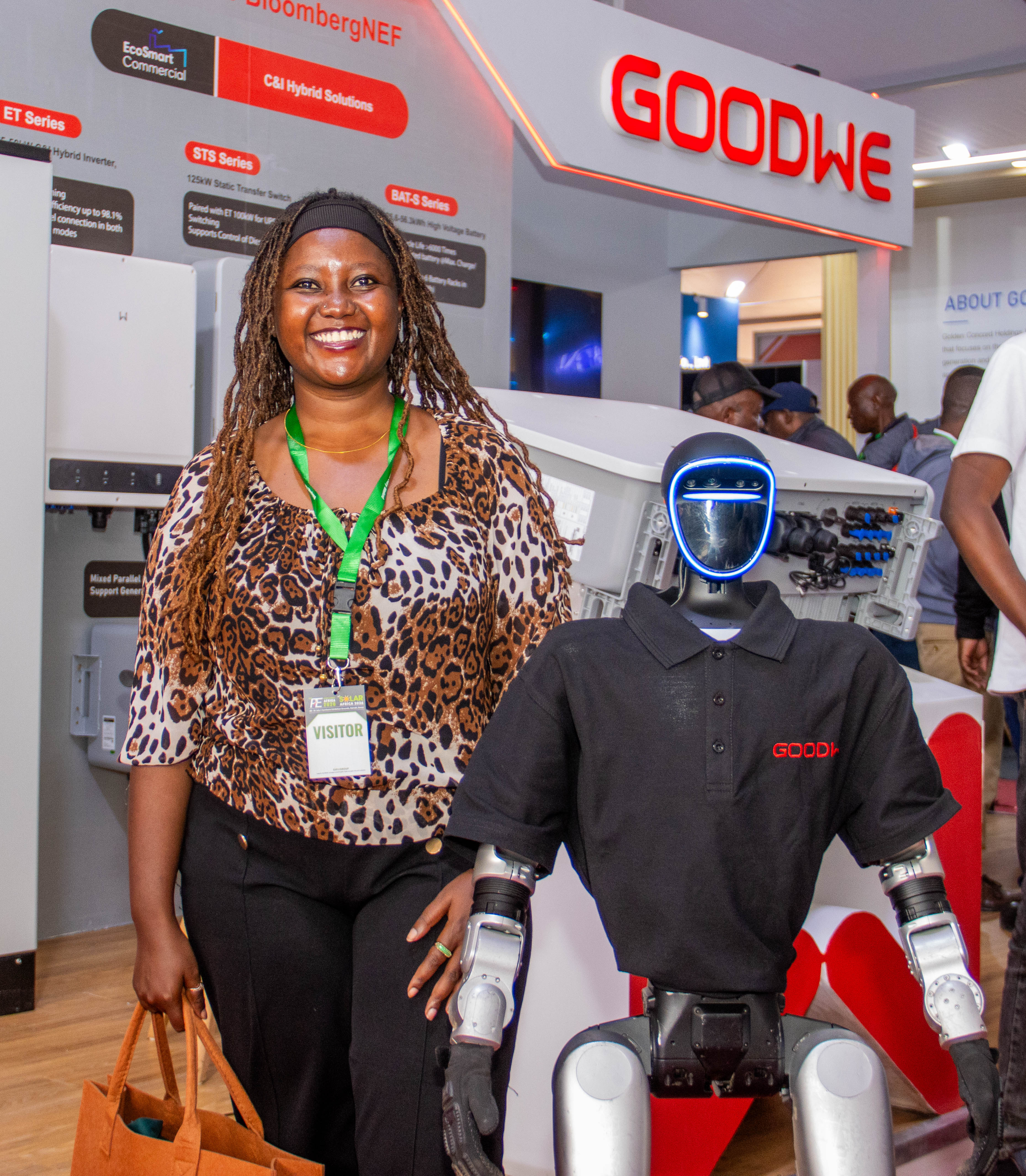 A smiling visitor with a lanyard poses next to a humanoid robot at the stand