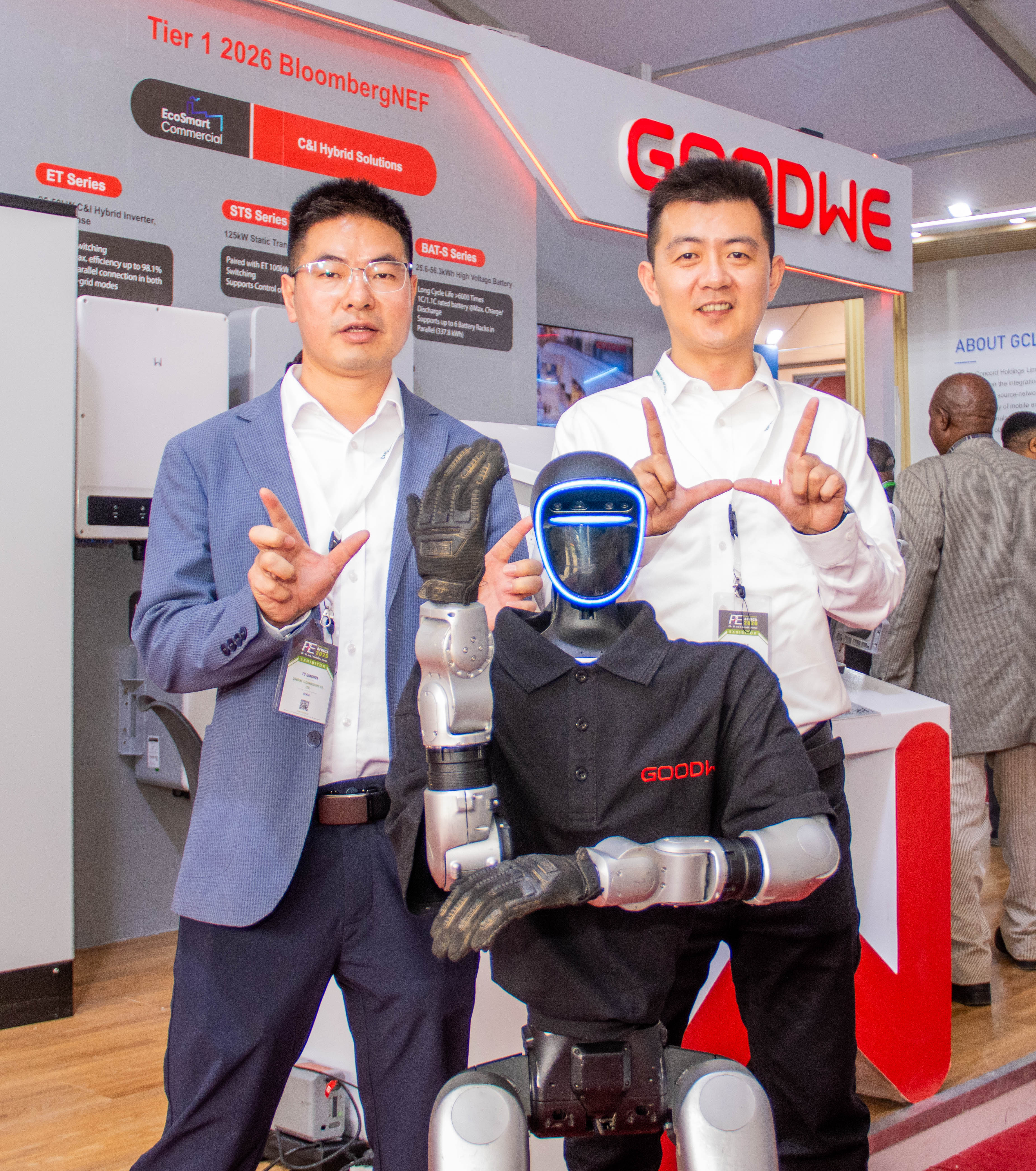Two men in suits make hand gestures beside a humanoid robot in front of the stand