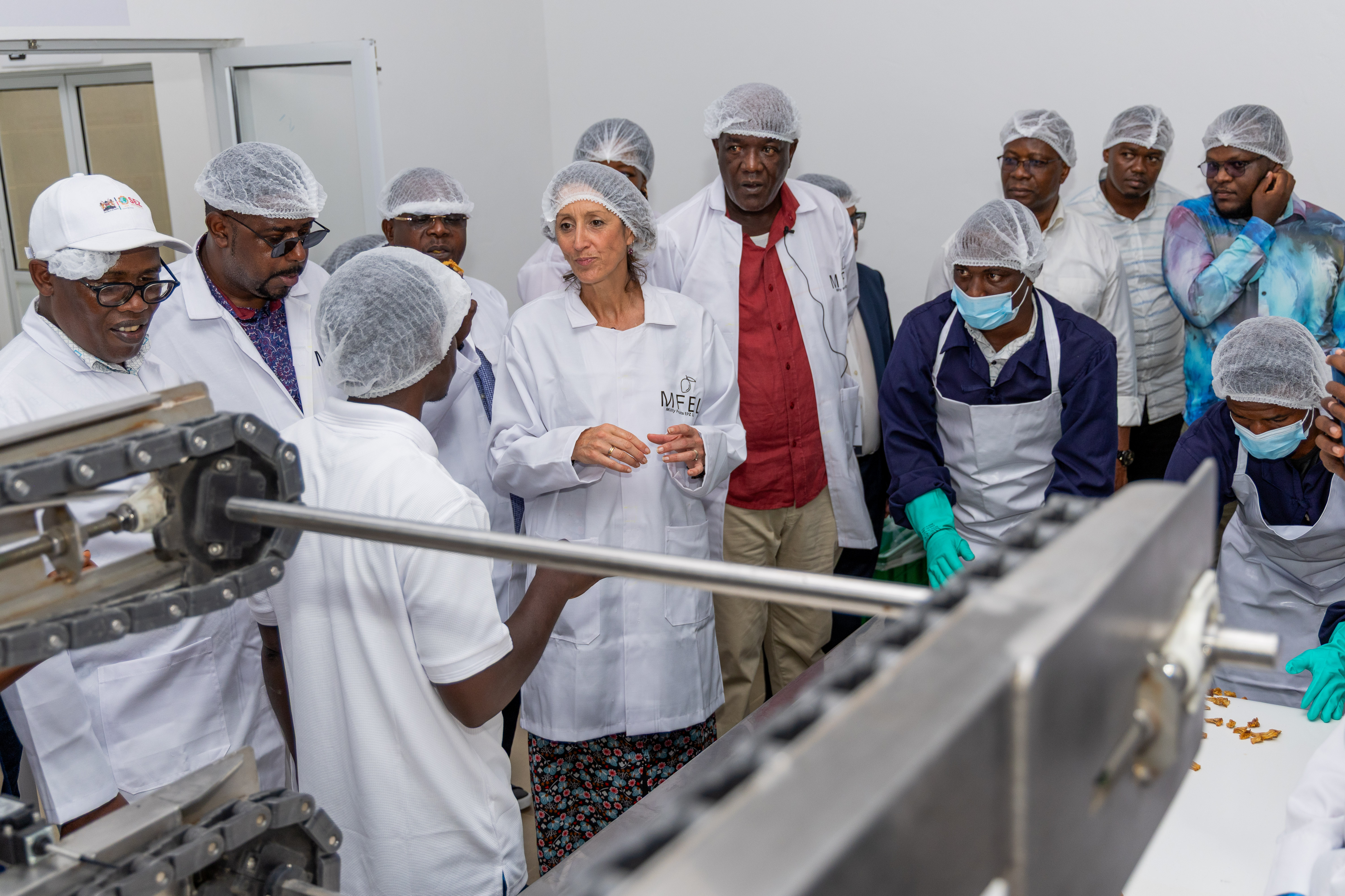Visitors in hairnets and white coats gather around stainless-steel processing machines