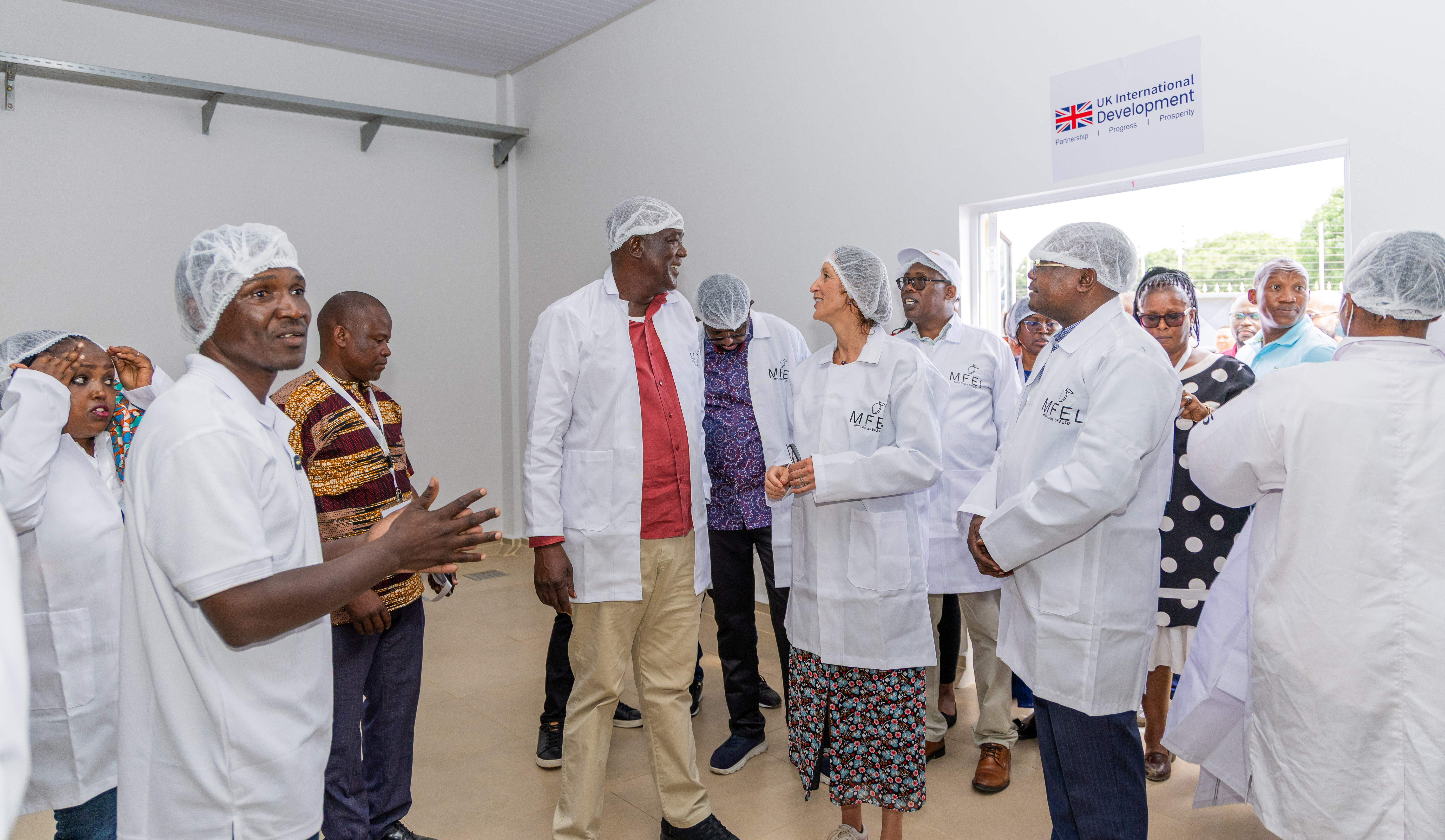 Guests in white coats and hairnets listen to a guide inside the factory