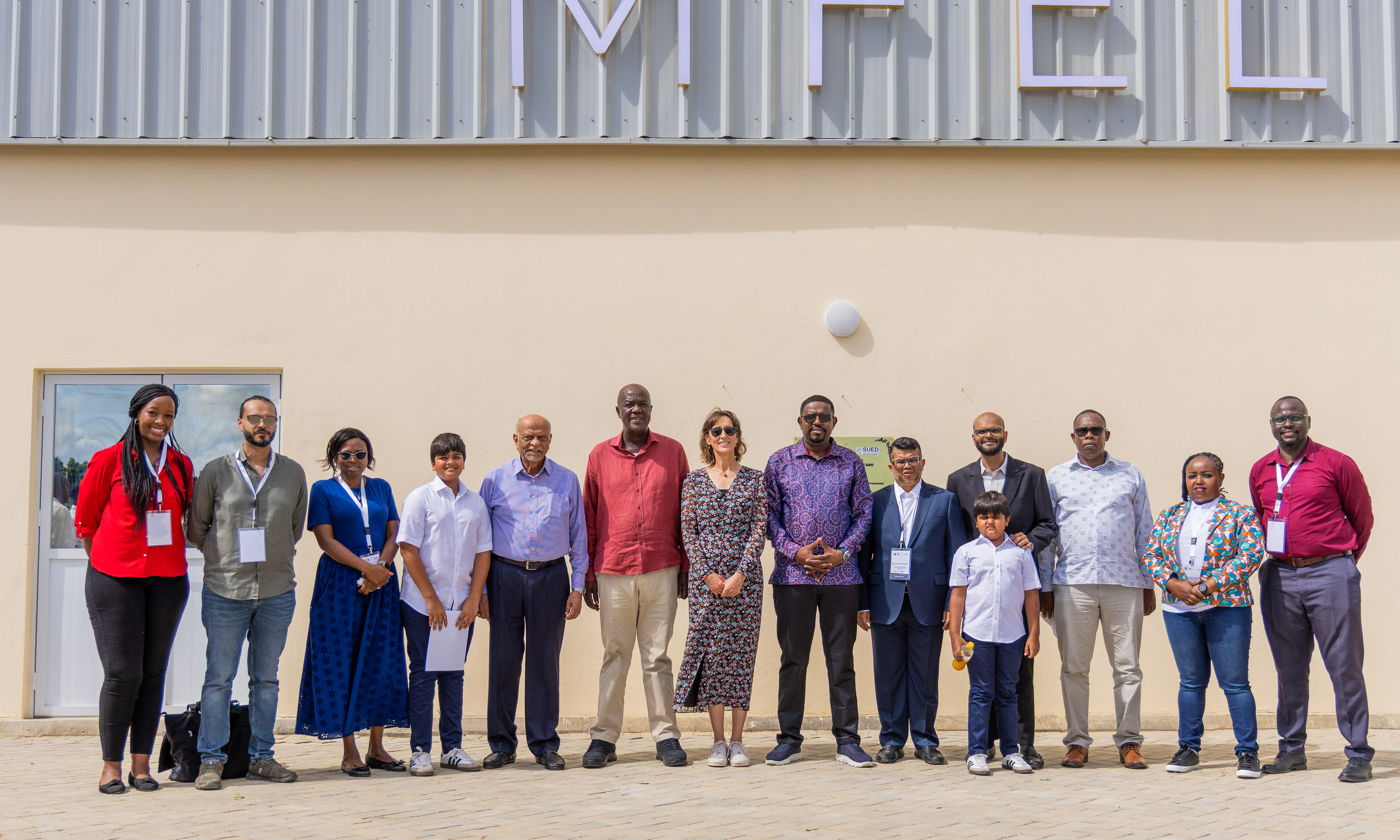 A group of guests and staff stand in a line in front of the new factory building