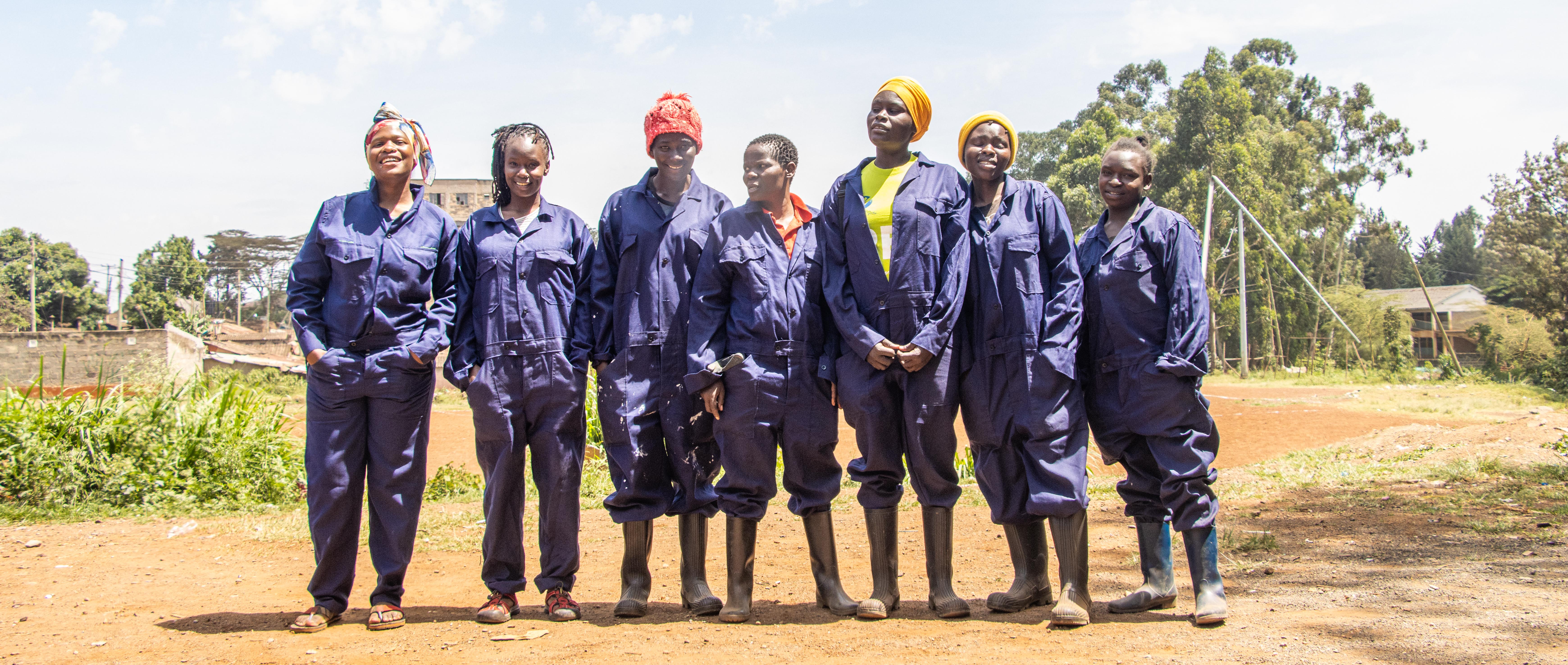 Seven members of a waste-collection group stand together in navy overalls and boots