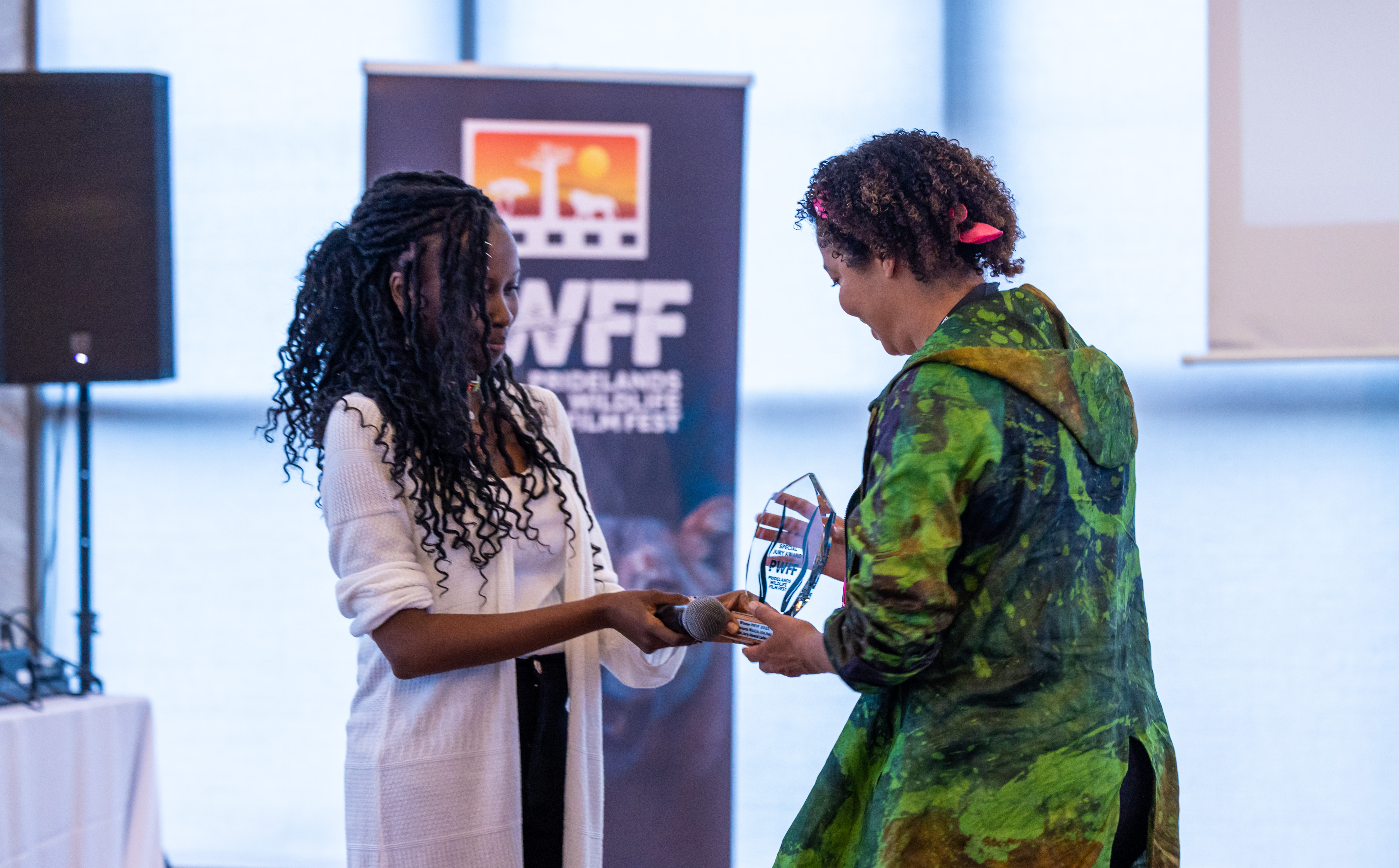 A woman presents an award to another woman in front of a festival banner