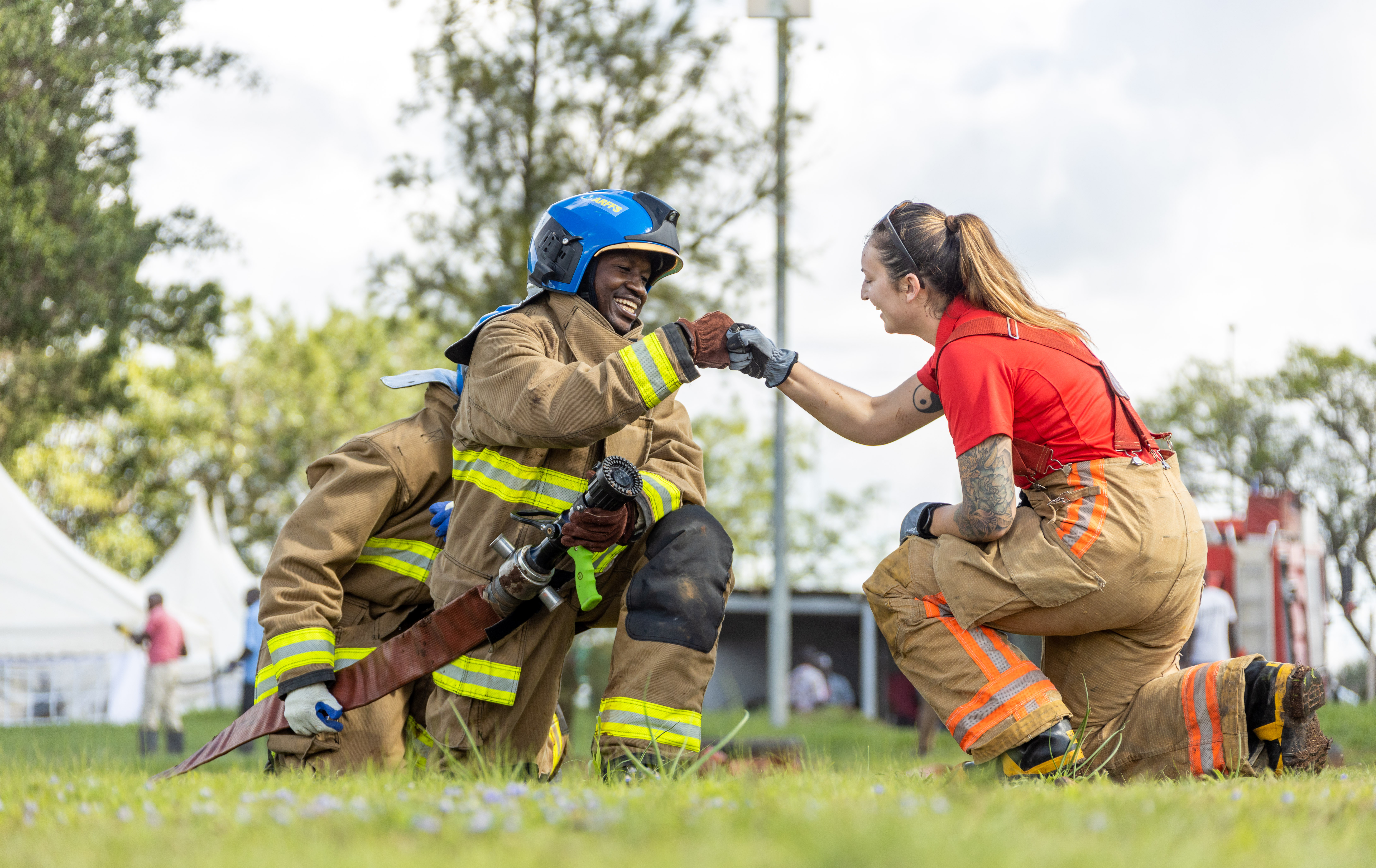 A firefighter in a blue helmet high-fives an instructor during a hose drill
