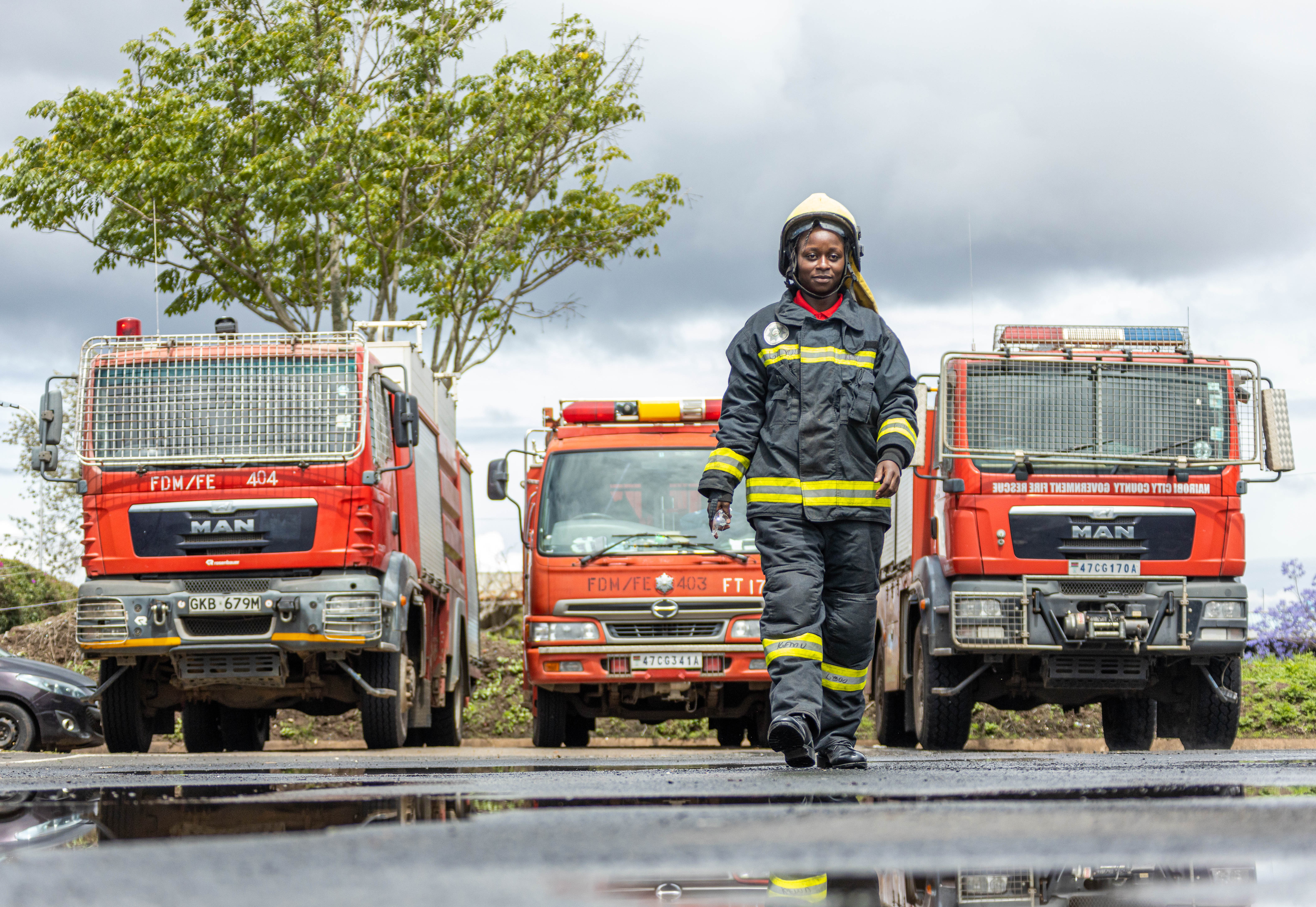 A woman firefighter walks toward the camera in front of three red fire engines
