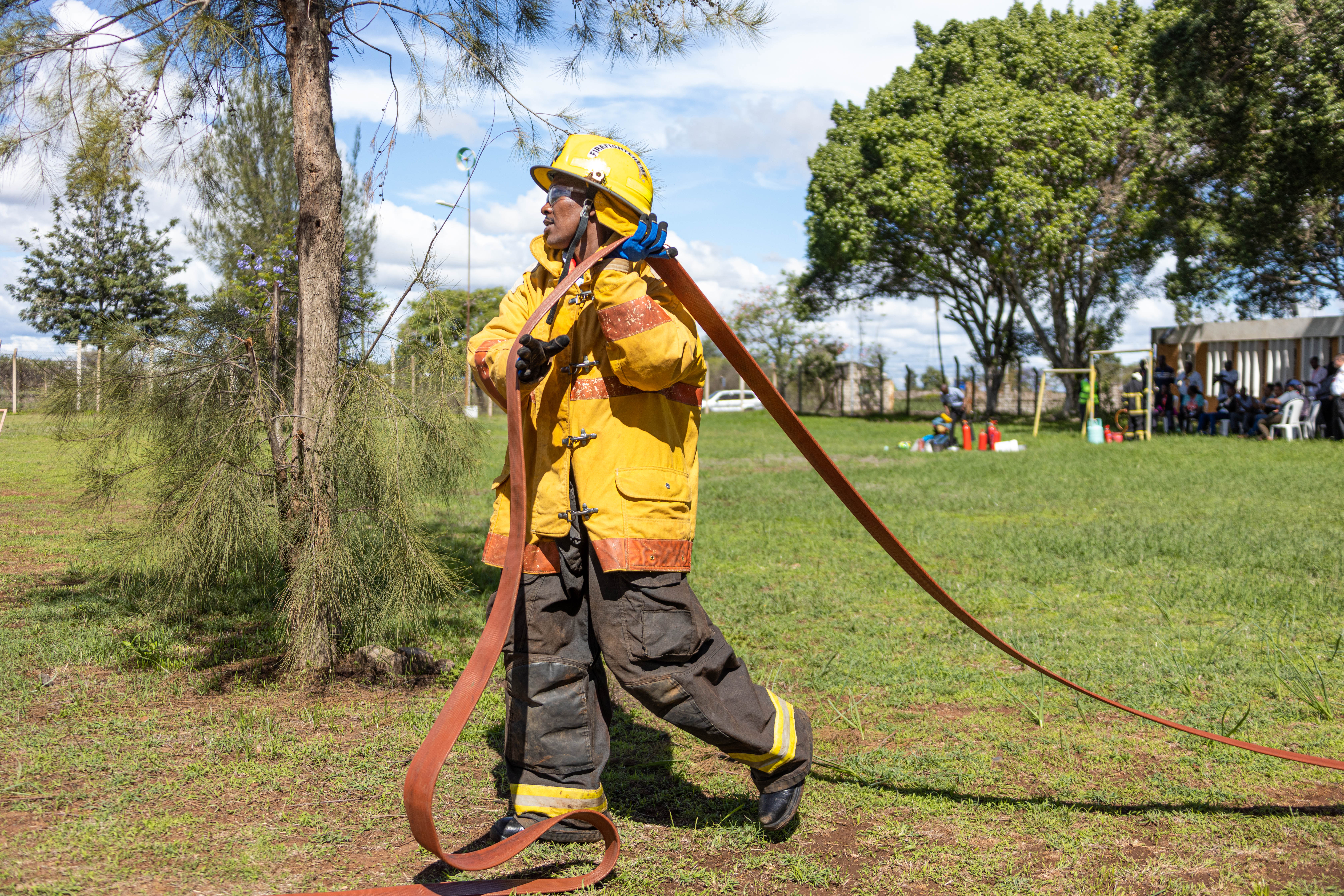 A firefighter in yellow gear drags a long hose line across a field