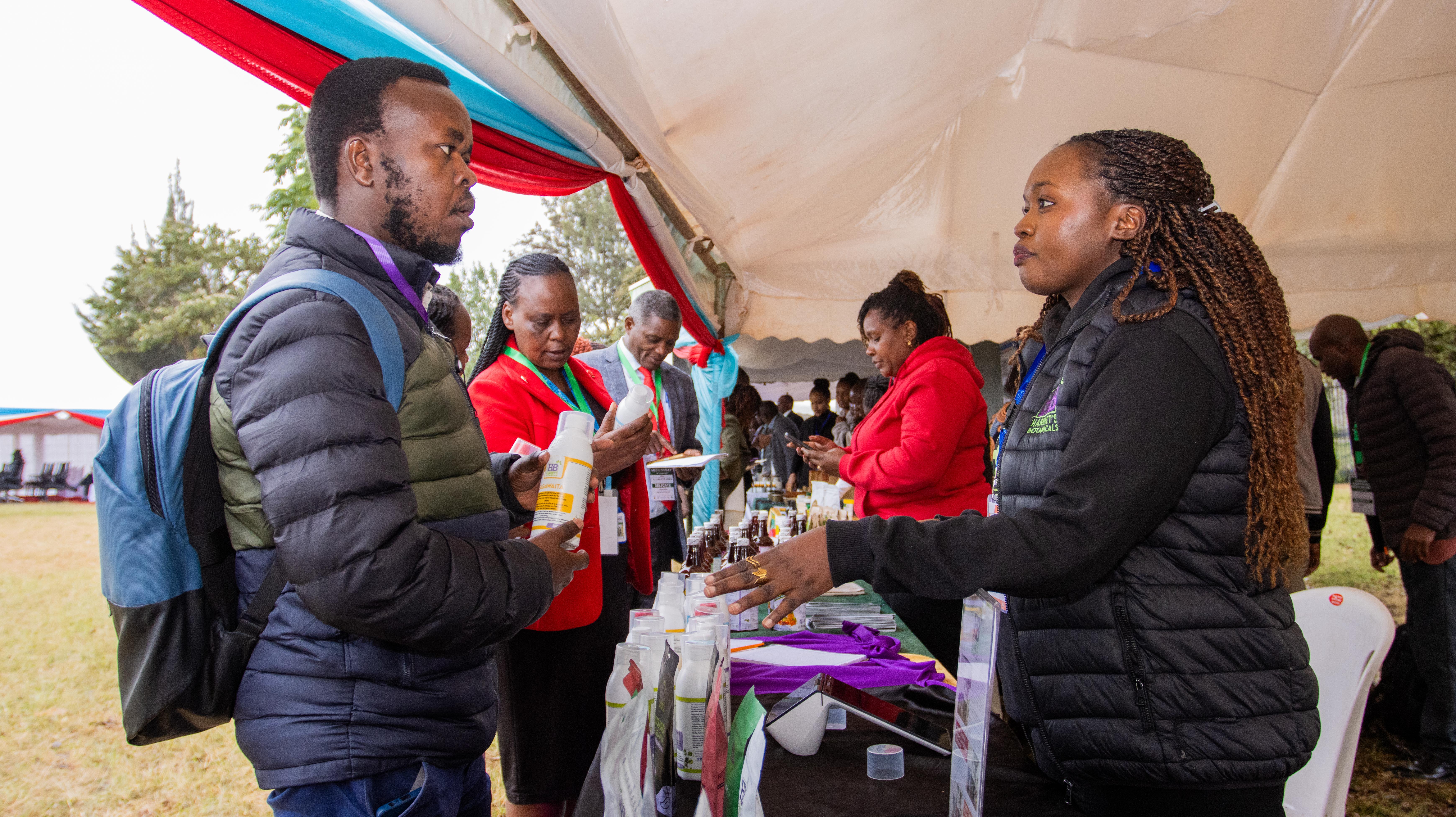 A visitor with a backpack examines a bottle held out by an exhibitor