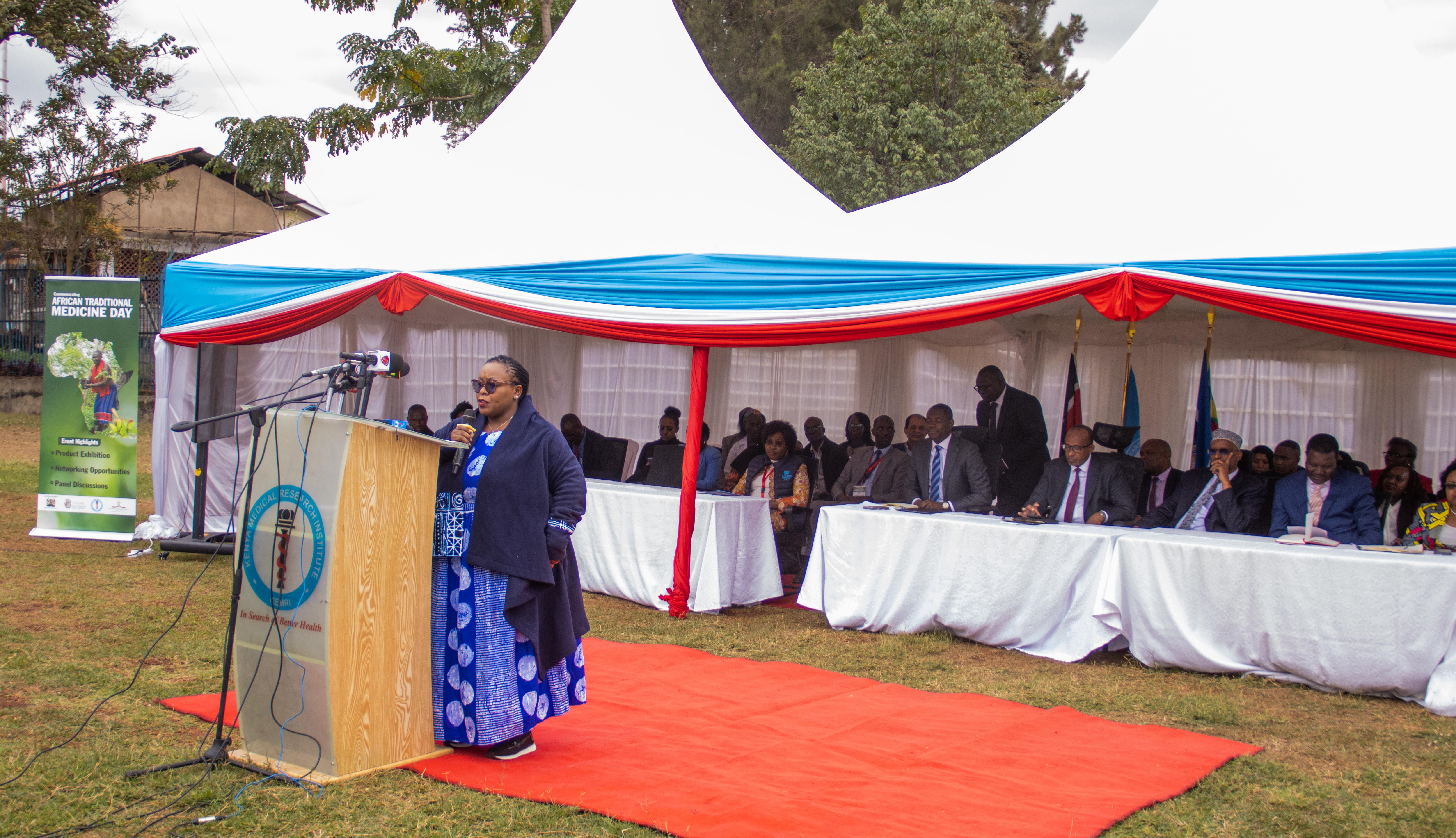 A speaker addresses guests from a podium on a red carpet under a white tent