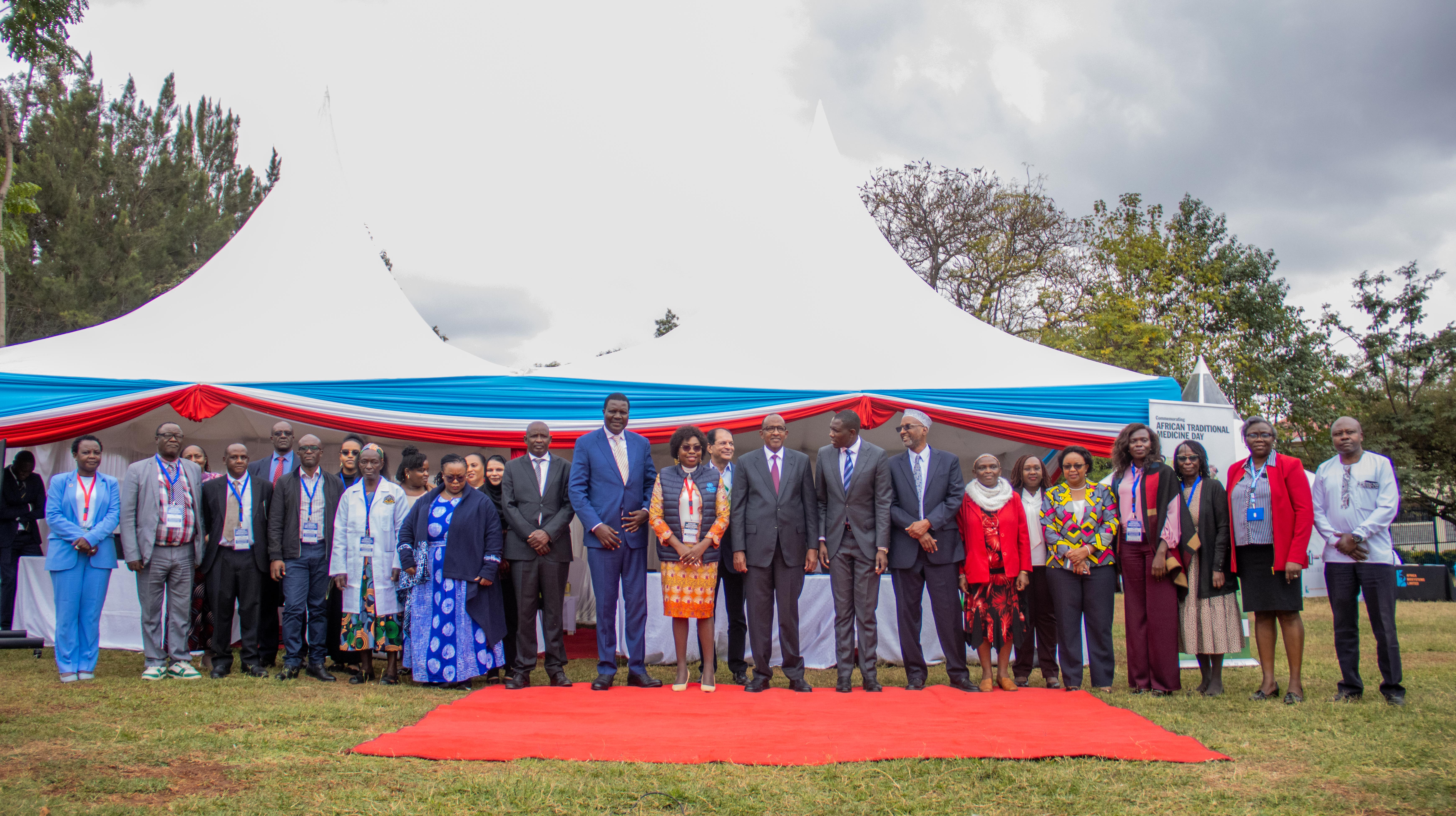 A large group stands for a photo on a red carpet in front of white tents
