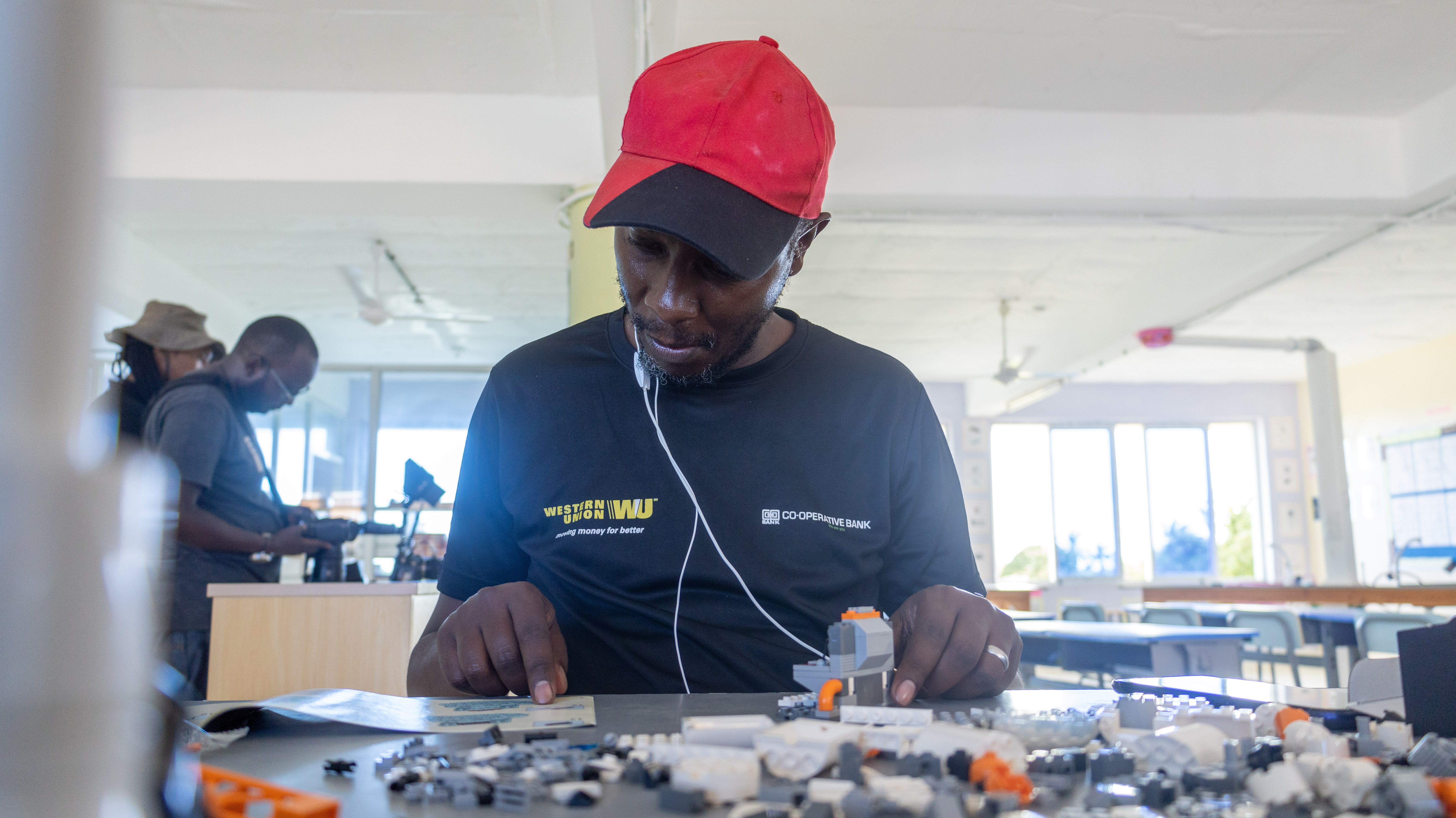 A man in a cap and earphones arranges small building pieces on a table